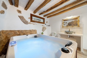 Un bagno con una vasca, un soffitto in legno, un muro in pietra, una finestra e uno specchio.