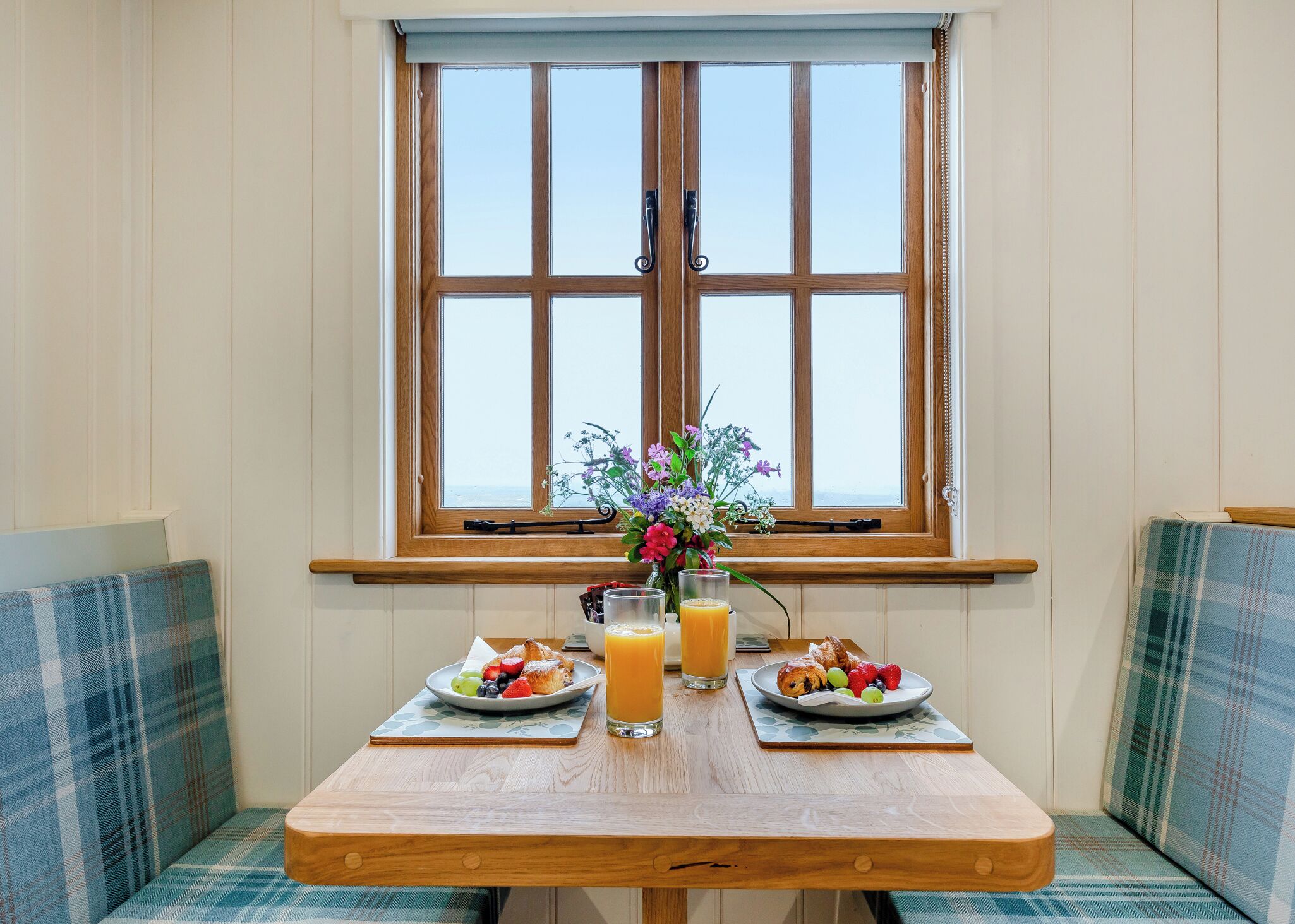 A breakfast table with two plates of food, a vase of flowers, and two glasses of orange juice.