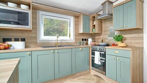A kitchen with a microwave, stove, sink, and wooden cabinets. - Diamond Caravan 3 Sleeps 6 (No Pet) (New Quay)