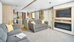 A modern living room with a sofa, a fireplace, and a TV mounted on the wall. - Diamond Caravan 3 Sleeps 6 (No Pet) (New Quay)