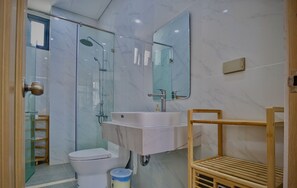 A modern bathroom with a glass shower enclosure, a white sink with a mirror above, and a wooden shelf.