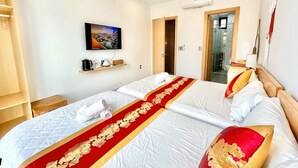 Une chambre d’hôtel avec deux lits, un téléviseur fixé au mur, une étagère avec des articles de toilette et une porte donnant accès à la salle de bain.