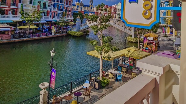 Une vue sur le front de mer, avec des bâtiments aux couleurs vives, une enseigne indiquant « Bien Coffee House Stay », et des tables à l’extérieur, près de l’eau.