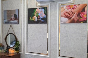 Une salle de spa avec des tableaux encadrés au mur, un miroir et une commode en bois où sont rangés les produits de toilette.