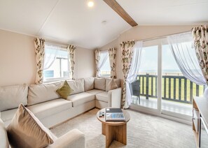A room with a beige sofa, a small wooden table, and a view of the ocean through large windows.