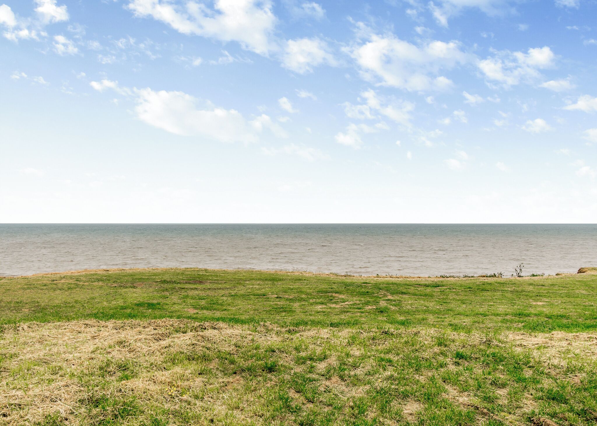 A grassy field with a view of the sea under a partly cloudy sky.
