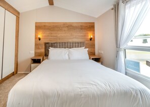 A bedroom with a wooden headboard, two bedside lamps, a large bed, and a window with curtains.