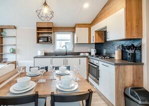 A modern kitchen with a dining area, wooden cabinetry, a built-in oven, and a gas stove. - This stunning holiday home with a double bedroom and en suite W. (Hornsea)