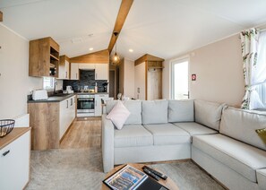 A compact living space with a kitchenette, a sofa, a coffee table, and a window with curtains. - This stunning holiday home with a double bedroom and en suite W. (Hornsea)