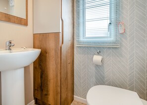 Une salle de bain avec un meuble-lavabo en bois, un lavabo blanc, des toilettes et une fenêtre avec des stores.