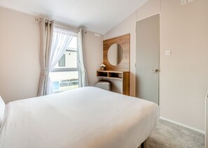 Une chambre à coucher avec un lit, une fenêtre avec des rideaux, un miroir et une porte.