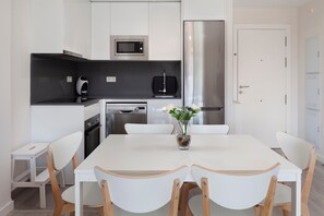 Una cucina moderna con mobili bianchi, un frigorifero in acciaio inossidabile, un forno a microonde e un tostapane.