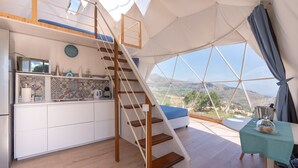 Alojamiento tipo tienda de campaña con cocina, una escalera de madera y un comedor con mesa y sillas.