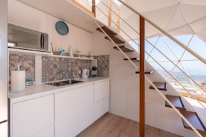 A kitchen with white cabinets, a microwave, a sink, and a coffee maker. There is a staircase with wooden steps leading to a balcony.