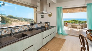 A modern kitchen with a large window, a dining area with a table and chairs, and a view of the ocean. - Sea view and direct access to the sandy beach (Sampieri)