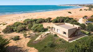 A modern building with a flat roof and a staircase on the side, situated near a beach with a clear blue sky. - Sea view and direct access to the sandy beach (Sampieri)