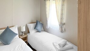 A hotel room with two beds, a nightstand with a lamp, and a window with patterned curtains. - Glenside 12 Superior (Hastings)