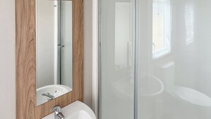 A bathroom with a wooden vanity, a white sink, a mirror, and a glass shower enclosure. - Glenside 12 Superior (Hastings)