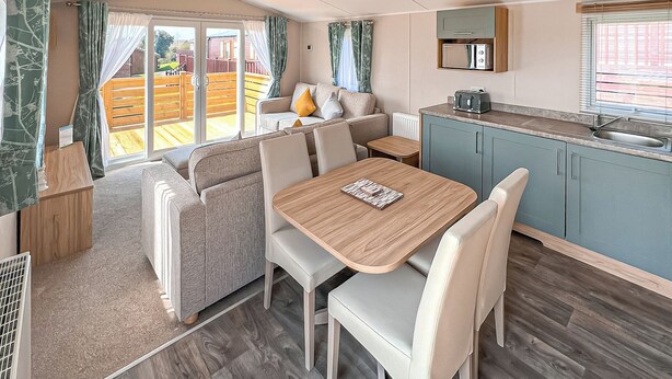 A caravan interior with a dining area, kitchenette, and a view of the outside. - Glenside 12 Superior (Hastings)