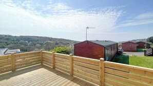 A wooden deck with a view of a red building and a hill in the background. - Glenside 12 Superior (Hastings)
