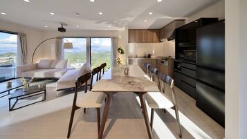 Una sala de estar moderna con comedor, cocina y ventanas amplias que ofrecen vistas panorámicas.