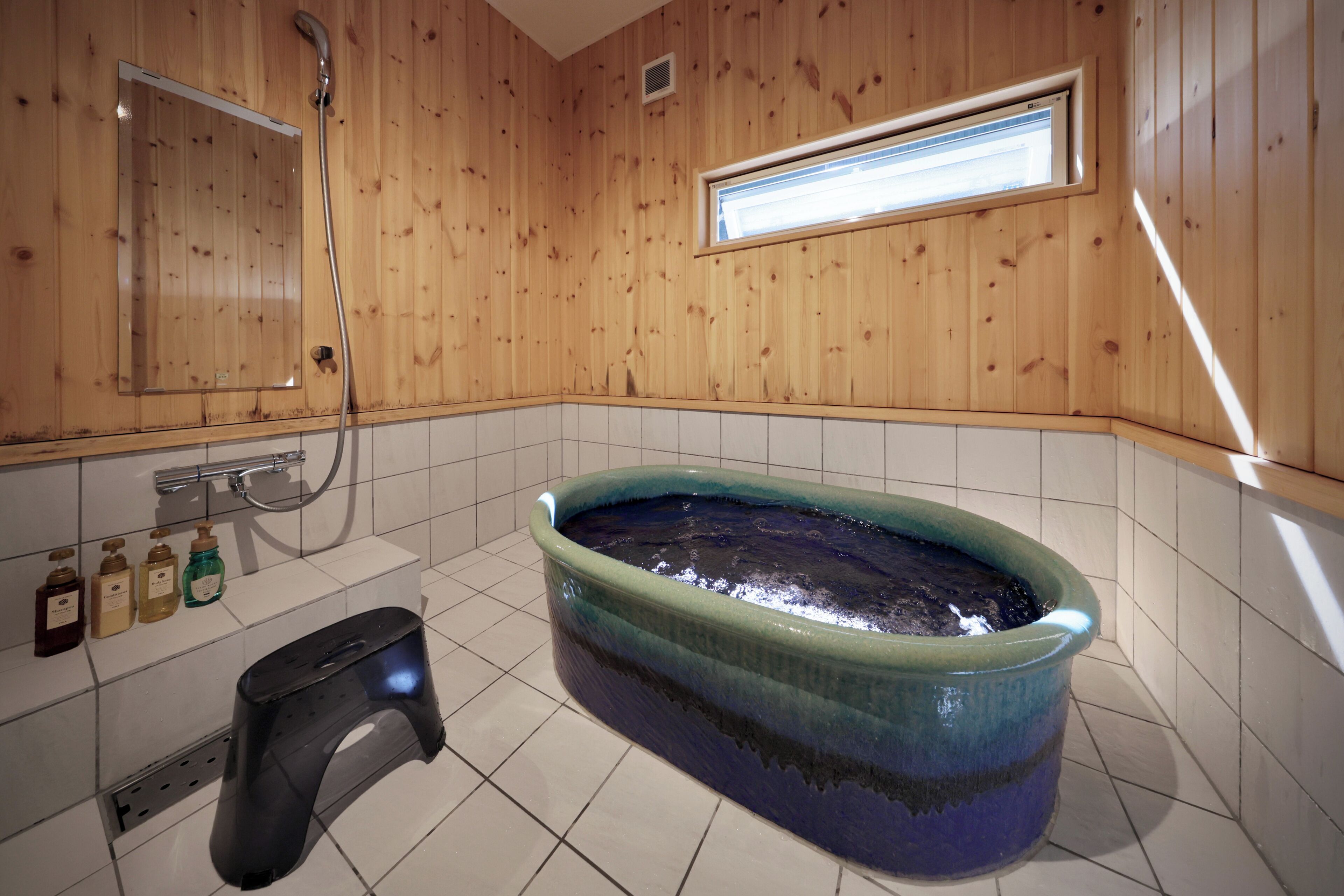 A bathroom with a wooden wall, a bathtub, a shower, and a window.