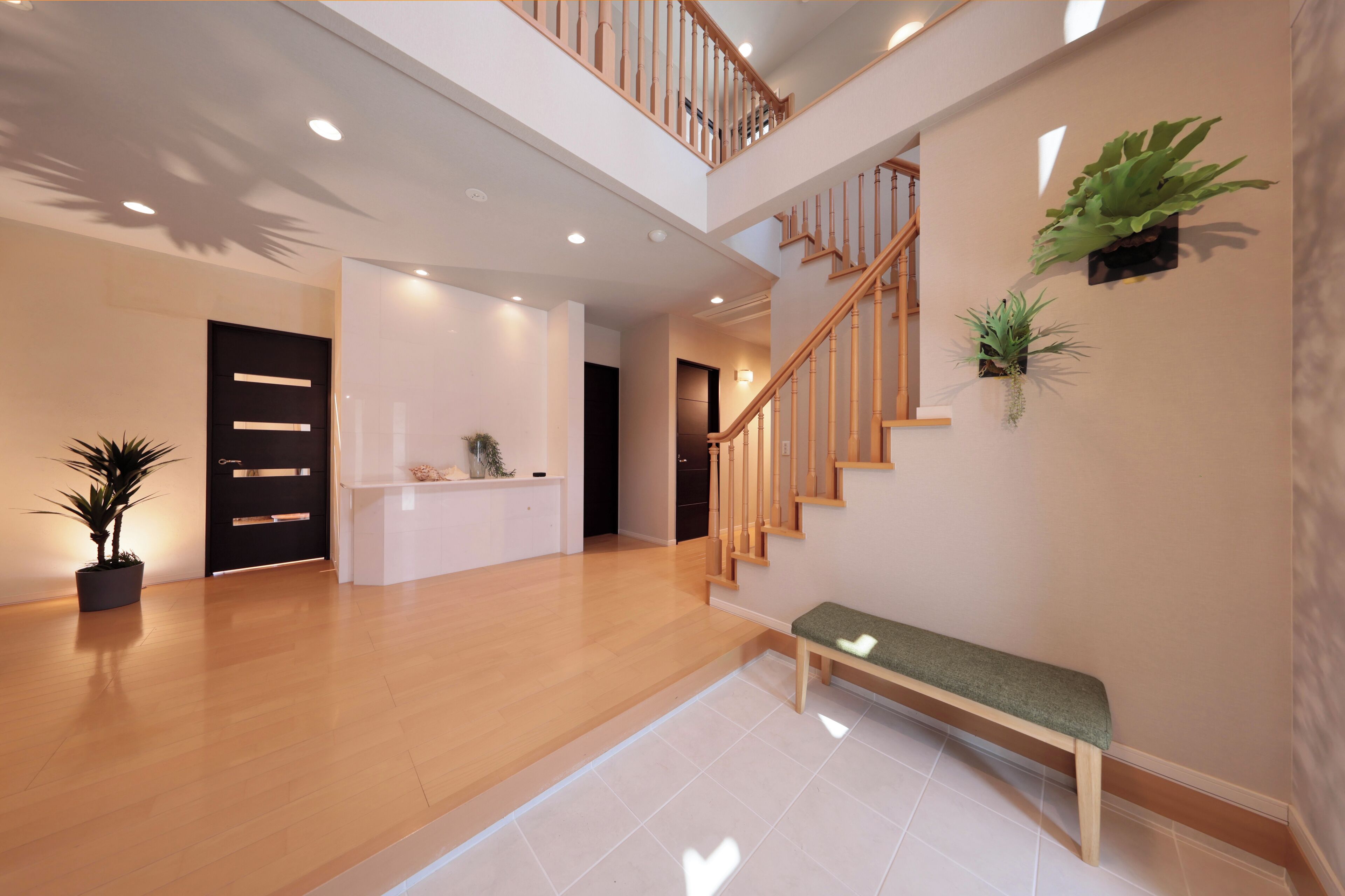 A spacious lobby with a wooden staircase, a reception desk, and potted plants.