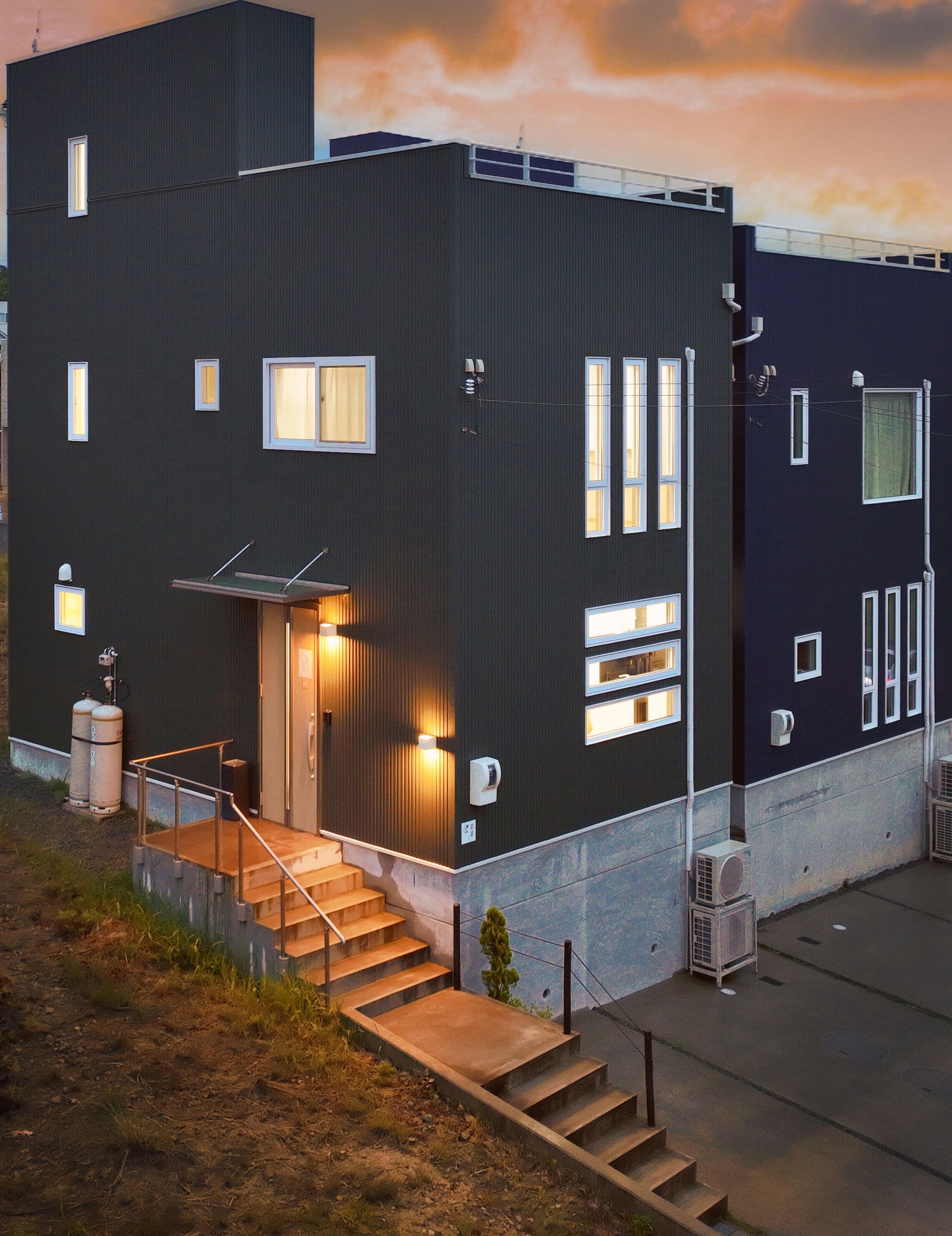A modern two-story building with a dark facade, multiple windows, and a staircase leading to the entrance.