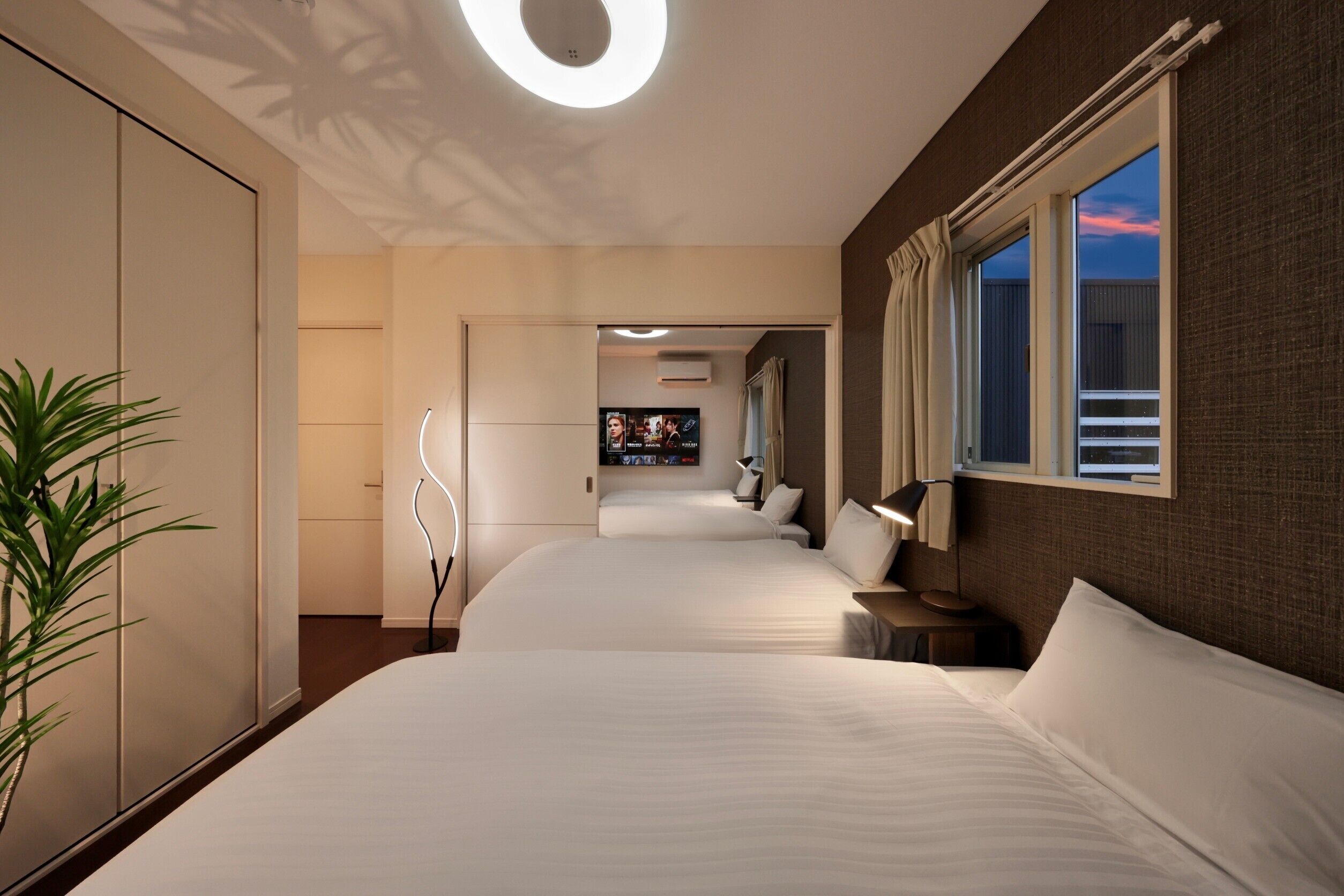 Een hotelkamer met twee bedden, een televisie, een plant en een raam met gordijnen.