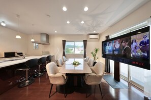 A modern dining area with a large table, bar stools, and a flat-screen TV displaying a movie. - Crystal Besso Shirahama (Shirahama)