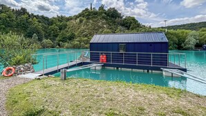 Une piscine avec un quai et un petit bâtiment, le tout entouré de verdure sous un ciel dégagé.