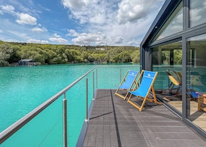 A deck with two blue lounge chairs, a glass railing, and a view of turquoise water and greenery. - 1 bedroom accommodation in Halling (Halling)