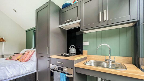 Une petite cuisine équipée, comprenant un évier, une cuisinière et un four, située à côté d’un lit avec des oreillers.