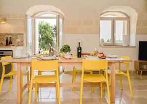 A dining area with a wooden table, yellow chairs, and a view of greenery outside. - Villa 'Trullo Delori with Infinity Pool' with Private Pool, Wi-Fi and Air Conditioning (Villa Castelli)