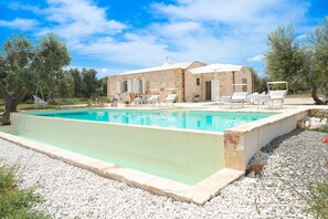 A swimming pool with lounge chairs, a stone building, and olive trees. - Villa 'Trullo Delori with Infinity Pool' with Private Pool, Wi-Fi and Air Conditioning (Villa Castelli)