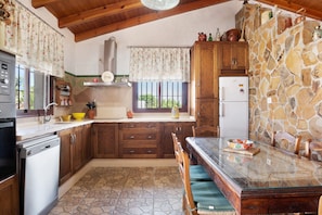 Een keuken met houten kasten, een stenen muur, een koelkast en een eettafel met stoelen.