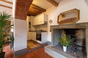 A kitchen with white cabinets, a stove, and a fireplace with a flower arrangement. - Casa Biffoli Apartment (Bucine)
