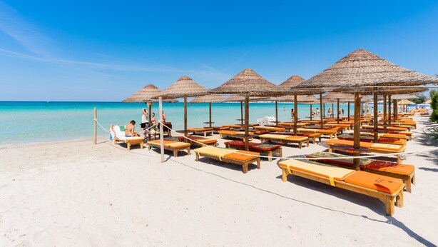 Een strand met ligbedden en rieten parasols.