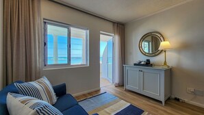 A room with a blue sofa, a white cabinet, a round mirror, and a view of the sea through large windows. - Blue Peter Hotel (Cape Town)