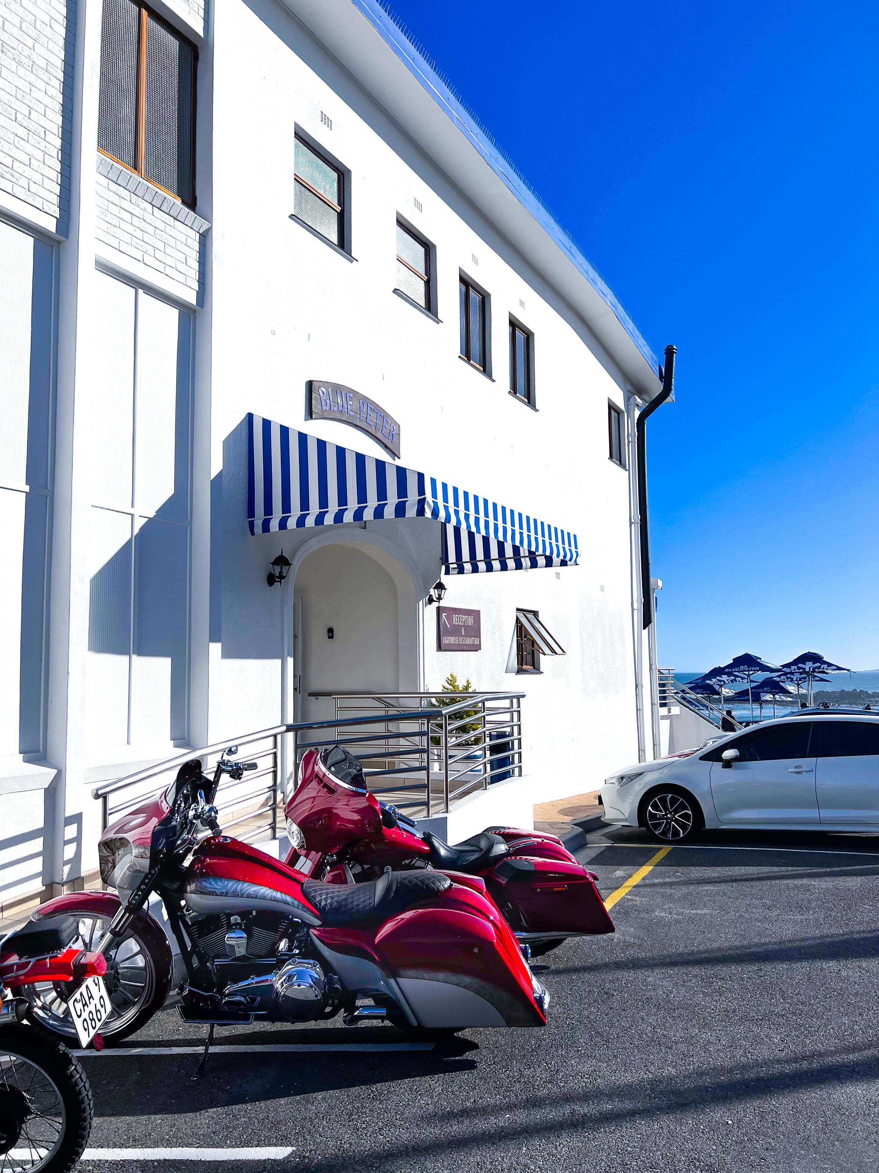 A building with a sign reading "BLUE PETER" and a blue and white striped awning. There are two motorcycles parked in front.