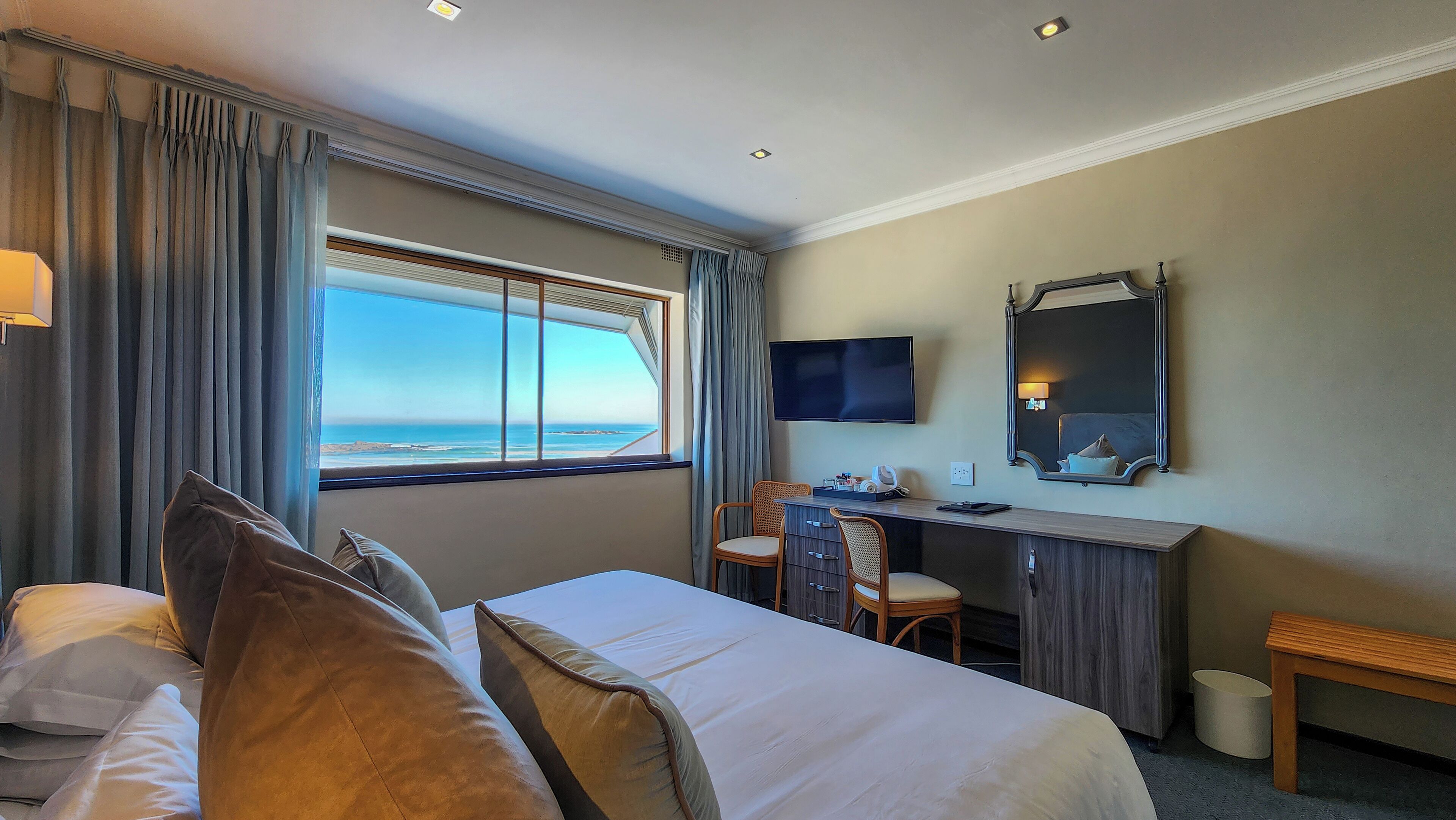 A hotel room with a bed, a desk, a chair, a television, and a large window with a view of the ocean.