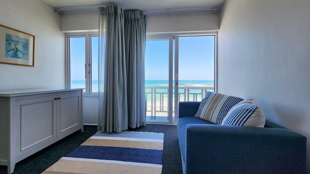 A room with a view of the beach, a sofa, a cabinet, and a striped rug. - Blue Peter Hotel (Cape Town)