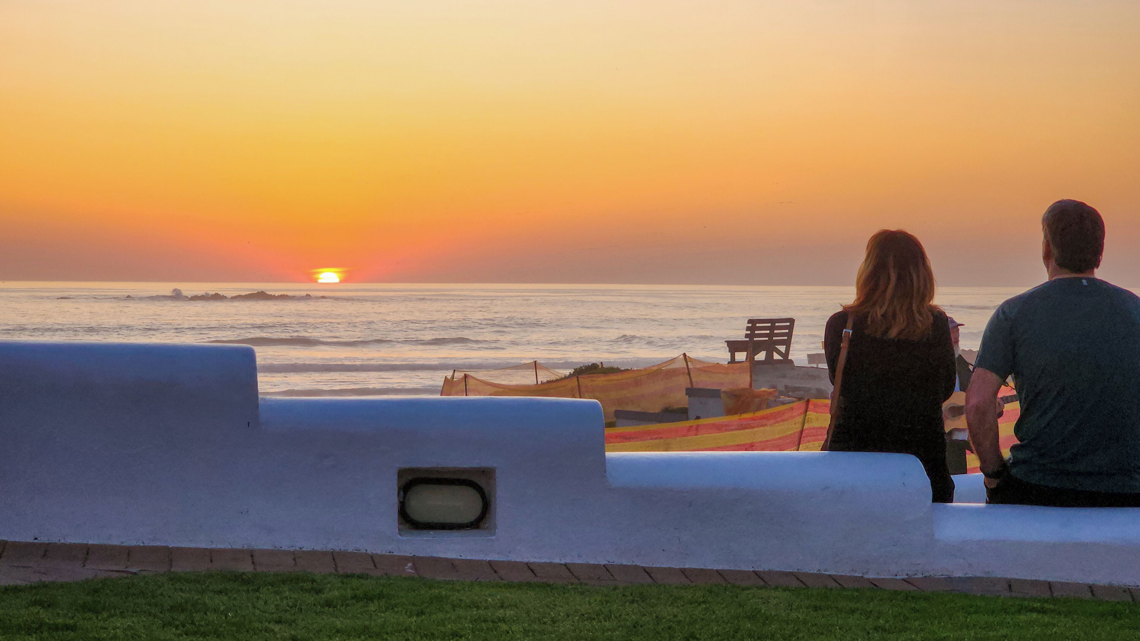 A couple sitting on a bench overlooking the ocean at sunset.