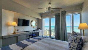 A hotel room with a bed, desk, TV, and a balcony with a view of the sea. - Blue Peter Hotel (Cape Town)