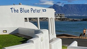 A coastal view with a sign reading "The Blue Peter" and a person in a red top looking out over the water. - Blue Peter Hotel (Cape Town)