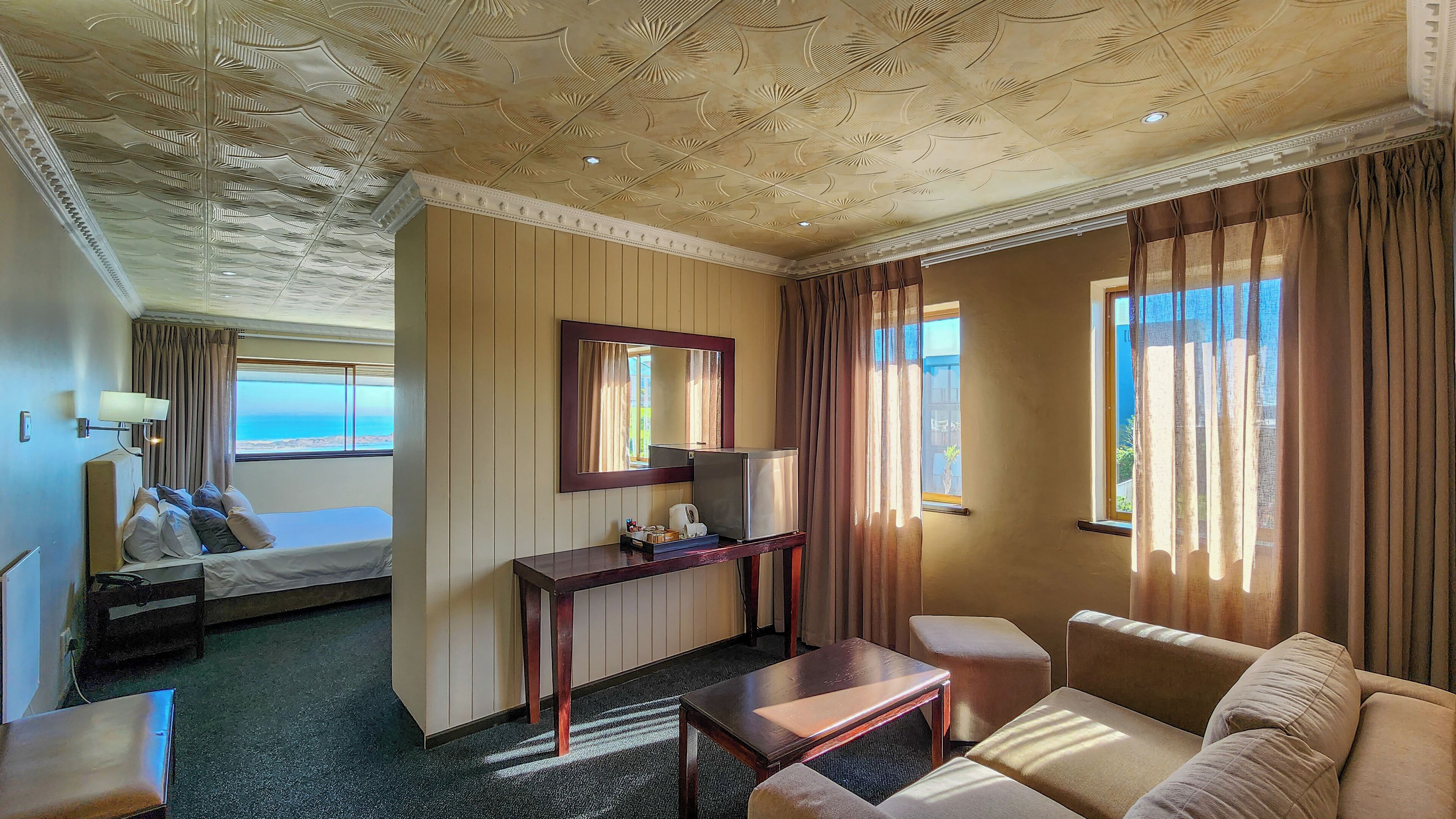 Hotelkamer met een bed, bureau met spiegel, een klein tafeltje en een bank. Er is uitzicht op zee vanuit het raam.