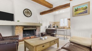 Un salon avec une cheminée, des meubles en cuir, une table basse en bois et, au fond, une cuisine.