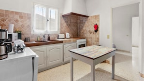 Une cuisine avec des meubles blancs, une fenêtre, une cuisinière et une table recouverte d’une nappe à rayures.