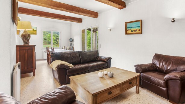 Un salon avec un canapé en cuir marron, une table basse en bois et un coin repas comprenant une table et des chaises en bois.