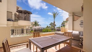 A balcony with a table and chairs, a covered seating area, and a view of palm trees and a building. - Seafront Apartment with Pool, Sea Views, Wi-Fi & Air Conditioning (Altea)